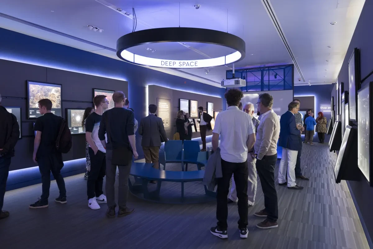 Image of many people standing around within a photography gallery with astrophotography images on the walls