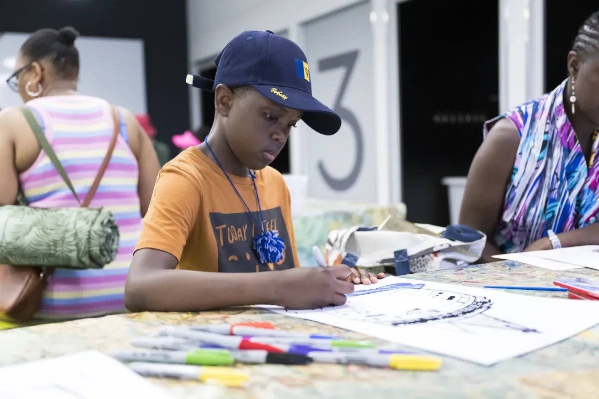 A boy in a baseball cap sits drawing during a craft activity