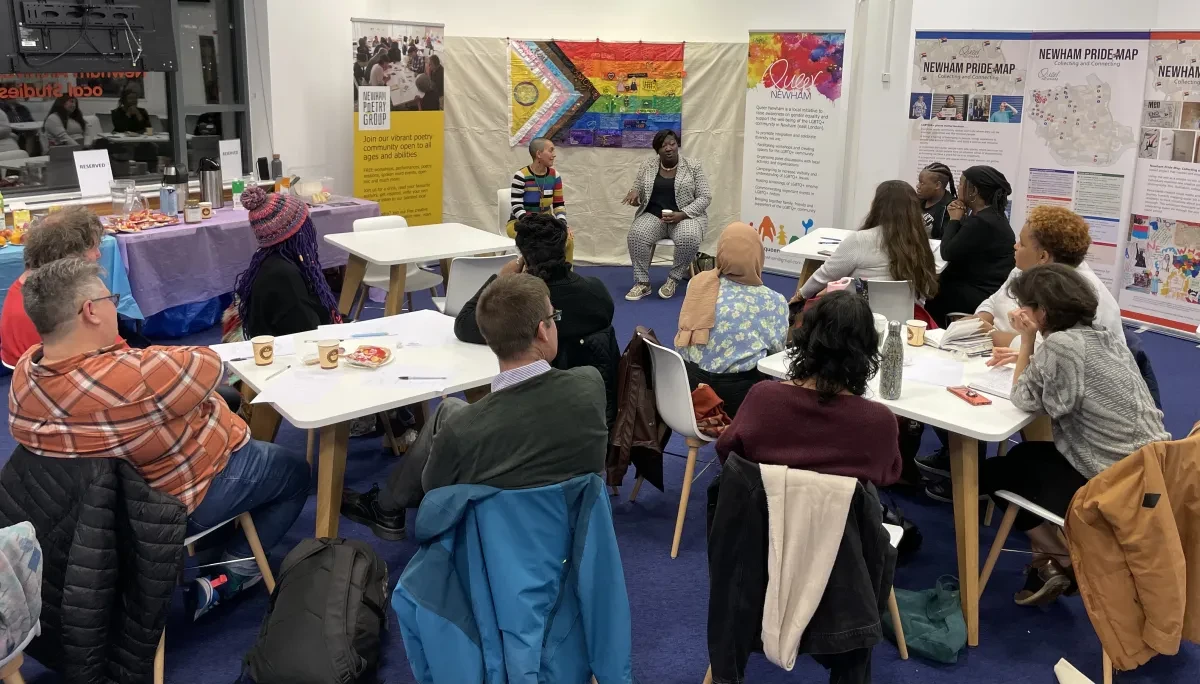 Photo of people sitting around tables listening to two people at the front of the room.
