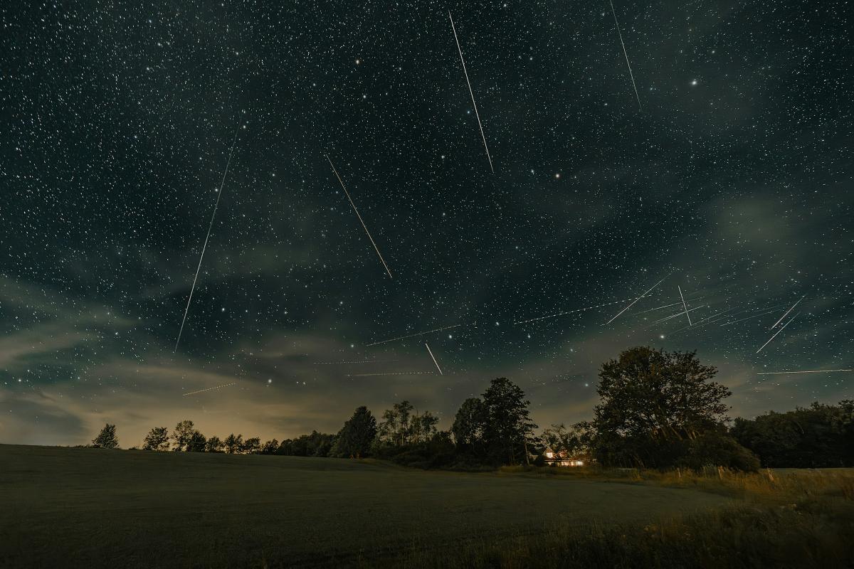 Photo of a landscape at night with streaks in the sky which are Perseid meteors raining down