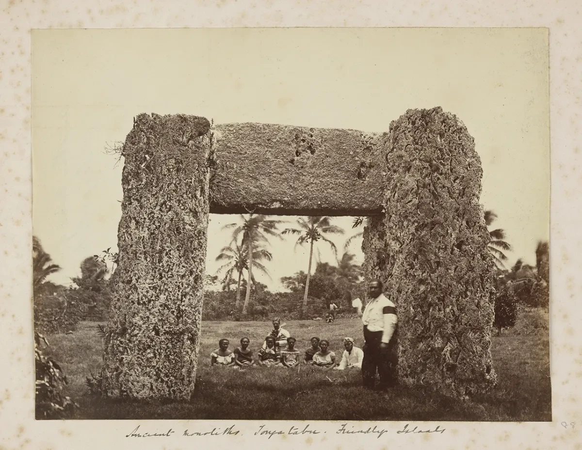 Historic photograph showing a group of Tongan women and men standing in the middle of the trilithon (stone arch) called Ha'amonga 'a Maui