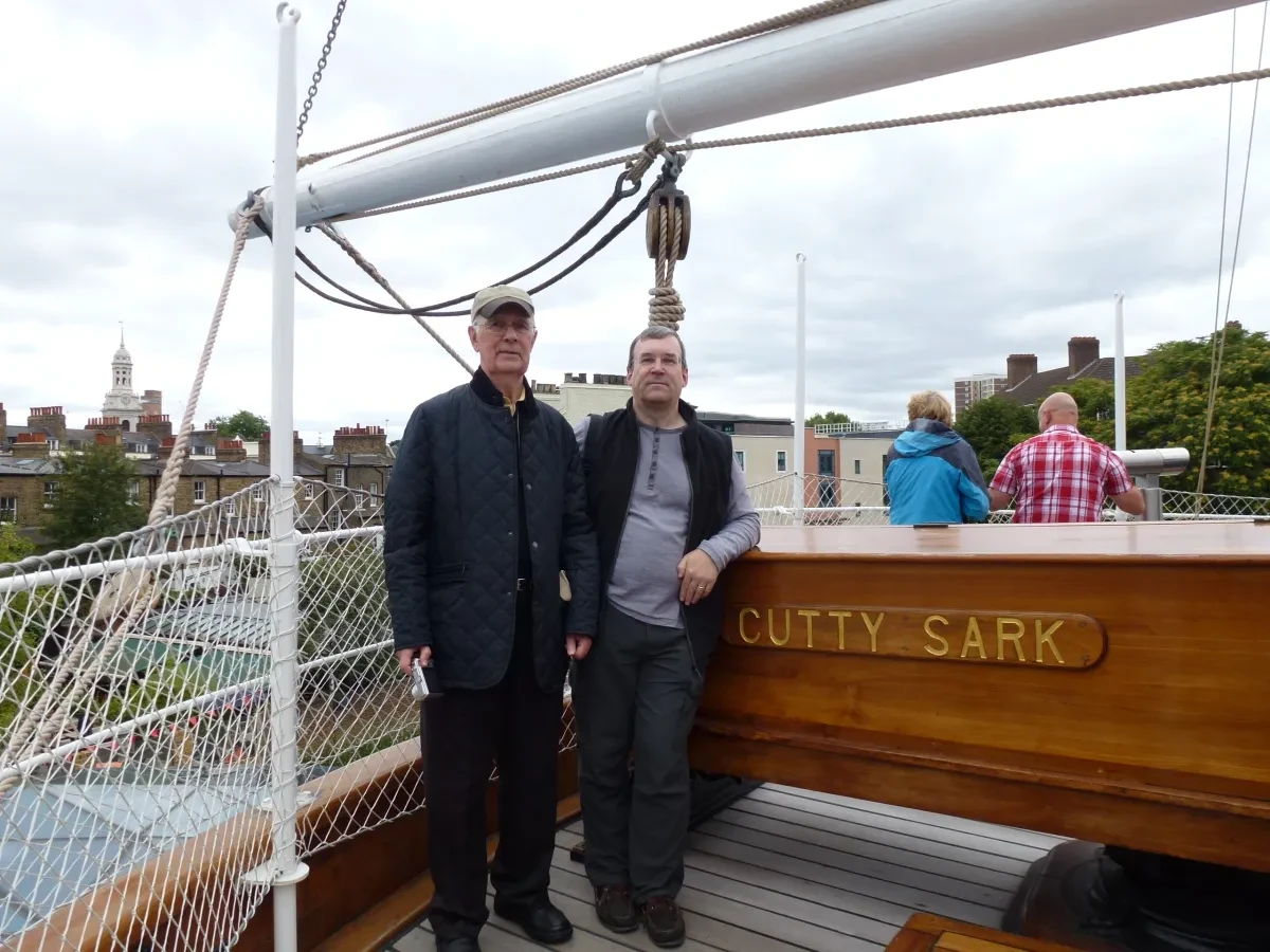 Two men stand side by side at the stern of historic ship Cutty Sark.
