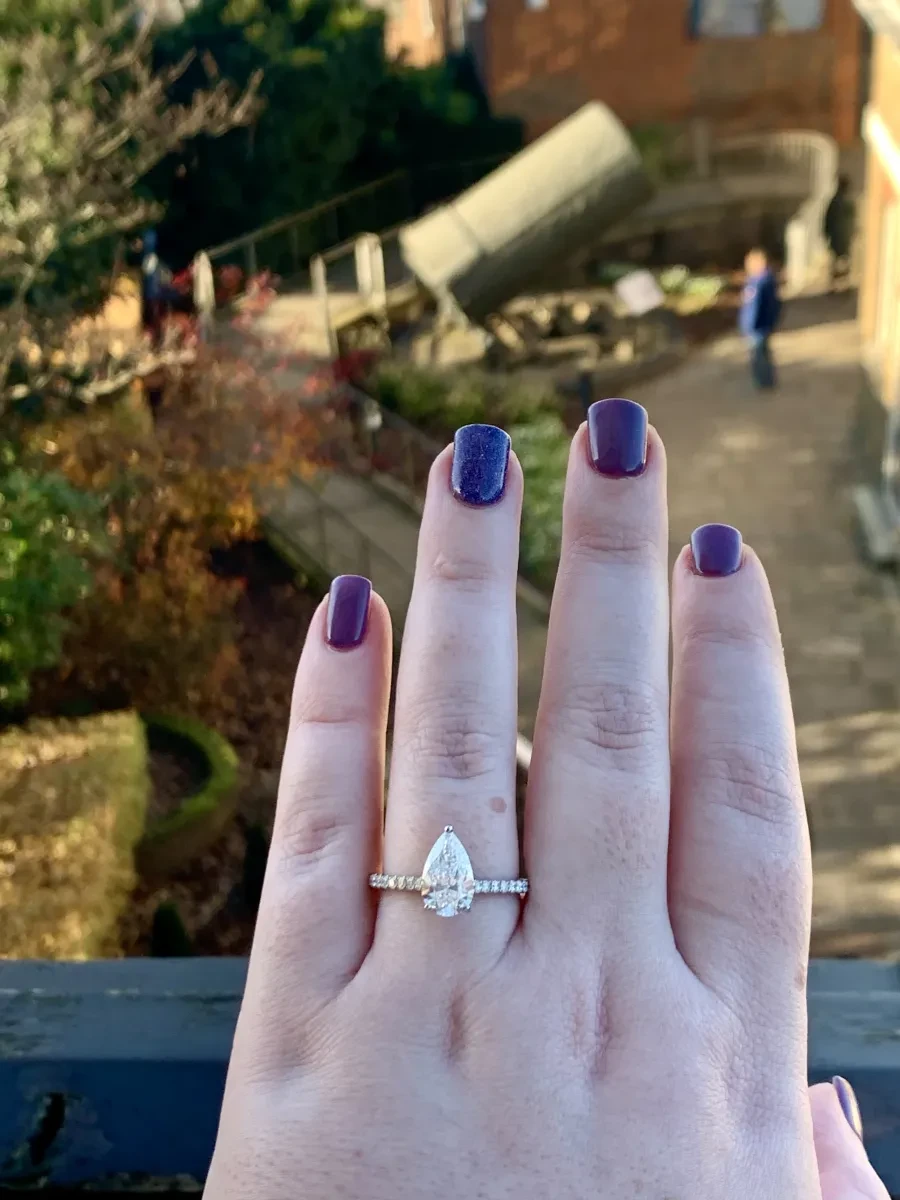 Close-up photo of a hand with a teardrop shaped engagement ring and purple painted nails.