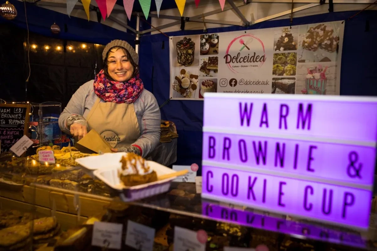 A female stallholder selling brownies smiles as she puts a sweet treat in a bag