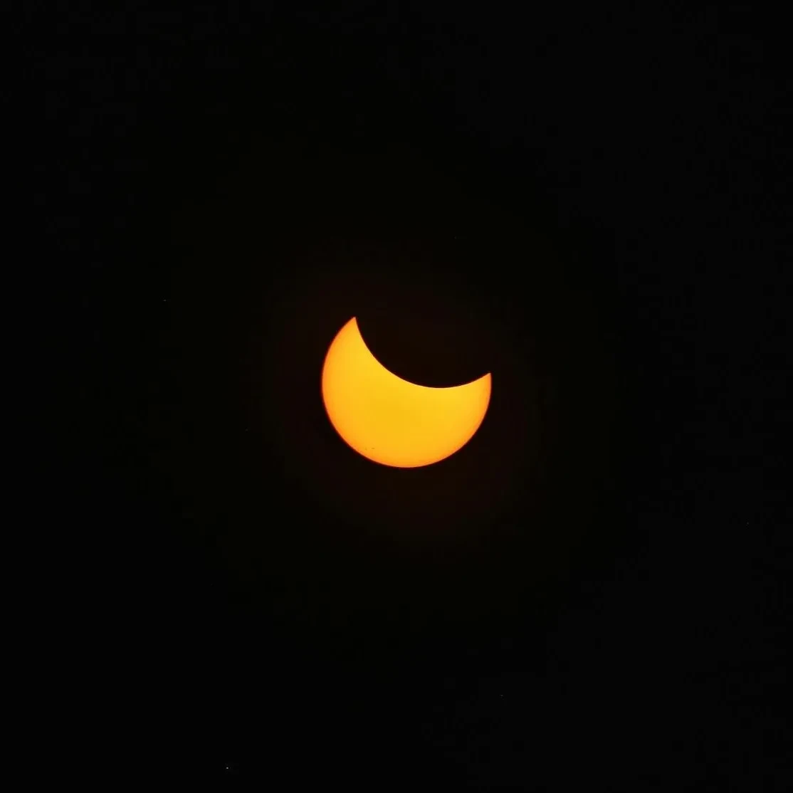 Thick yellow crescent of the Sun with a circular section missing in the top right corner against a black background
