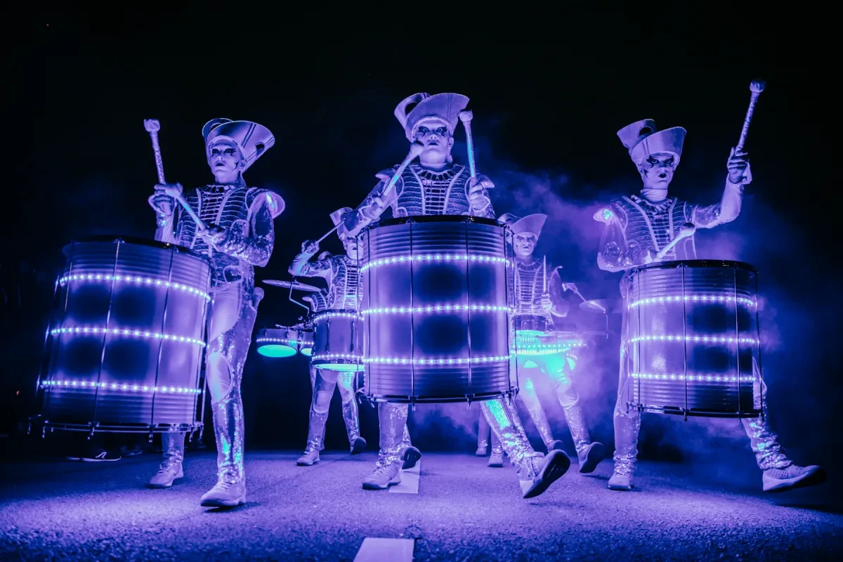 A group of drummers wearing eerie costumes and lit with flashing purple light
