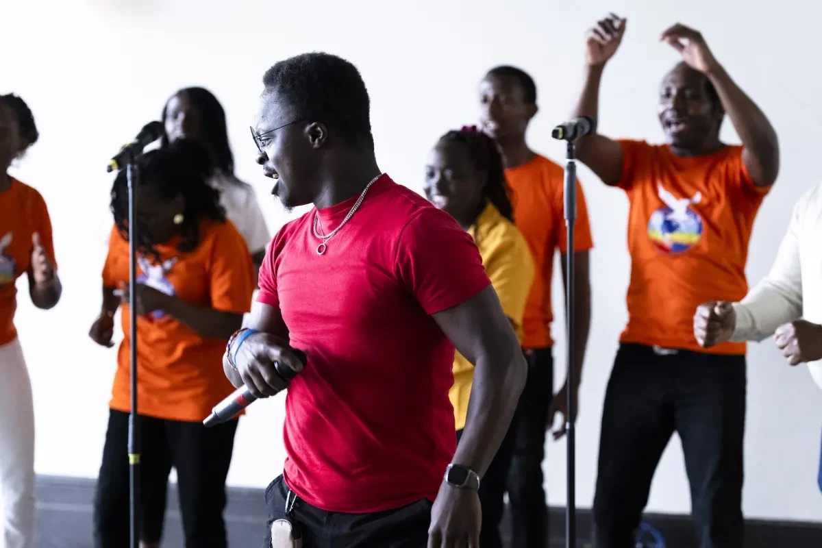 A group of singers performing. The group are wearing red, orange and yellow t-shirts