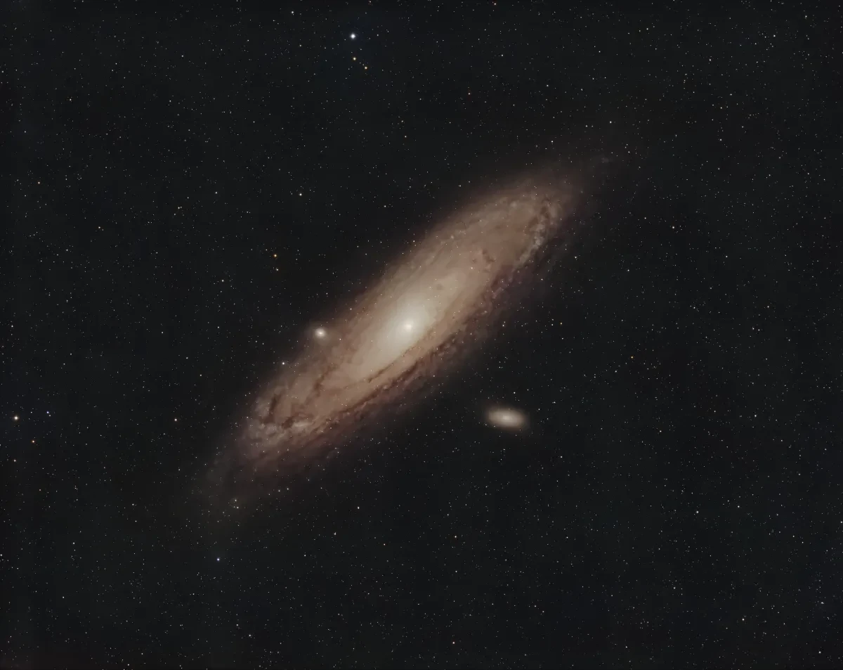 Photo of Andromeda Galaxy, a diagonal spiral galaxy in pale dusty brown hues, against black sky