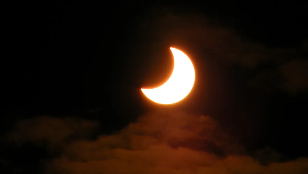 Photo of Sun in dark cloudy sky which is 30% hidden by the Sun