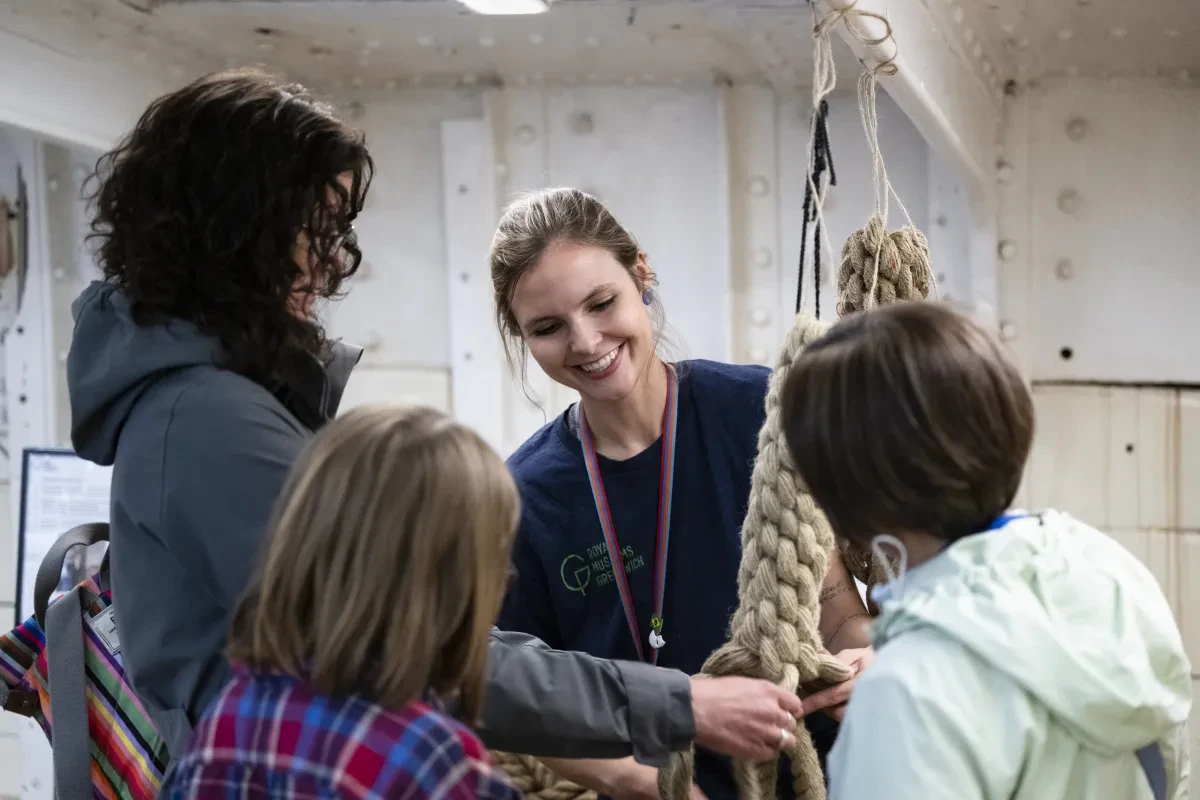 Photo of woman wearing navy top and coloured lanyard smiling as she shows three people a piece of coiled and knotted rope