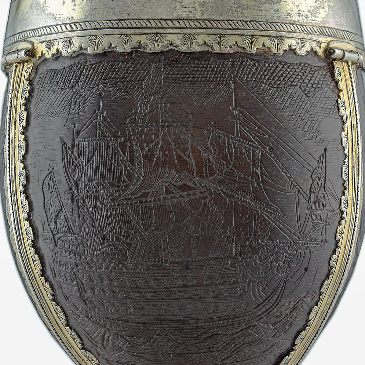 A carved coconut shell set within a silver frame and handle. The shell acts as the bowl of a highly decorative cup