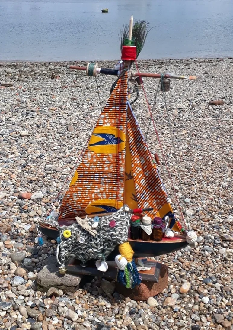 a handmade model boat with a colourful sail on a stony shore
