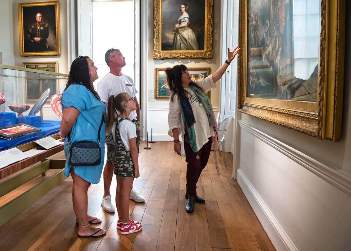 A woman points out something of interest in a painting to a family group