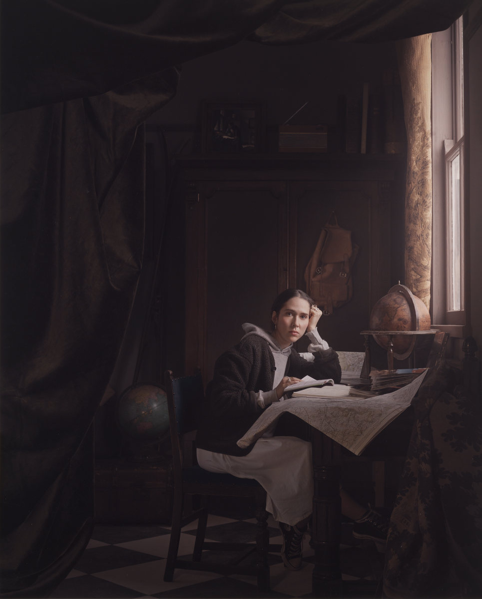 A woman leans over her desk in a setting inspired by a 17th century Dutch room