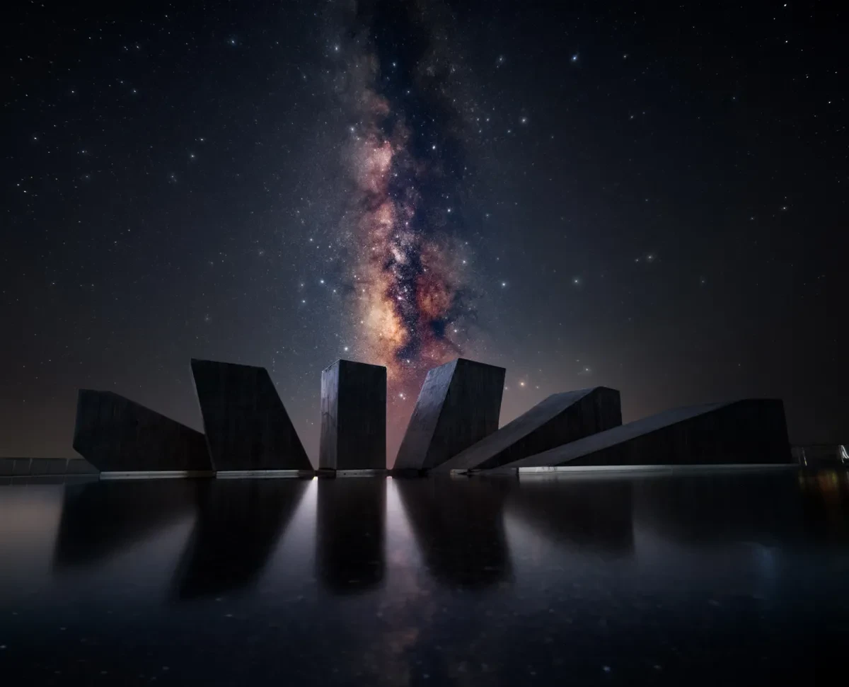 Vivid Milky Way core vertical in sky over sculpture of black stones with water in foreground