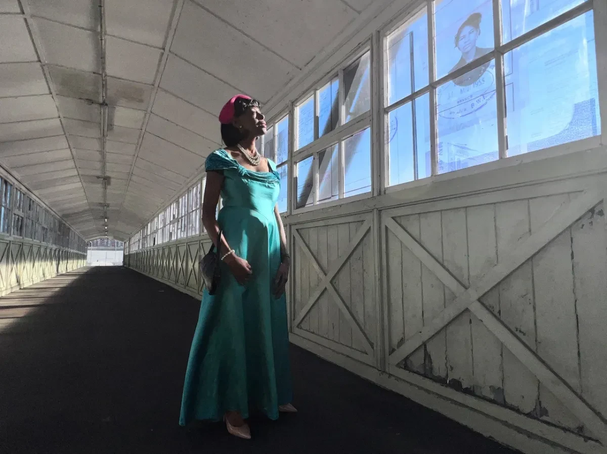 Still from Here I Stand showing woman in long green dress on Tilbury Bridge walkway