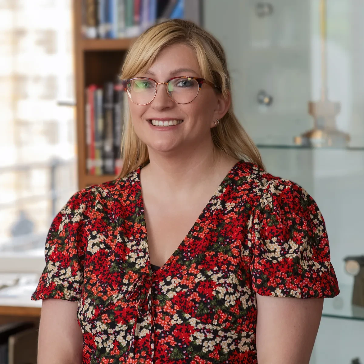 Astronomer Liz Avery smiling warmly. She has blonde shoulder-length hair, and is wearing glasses and a red patterned dress