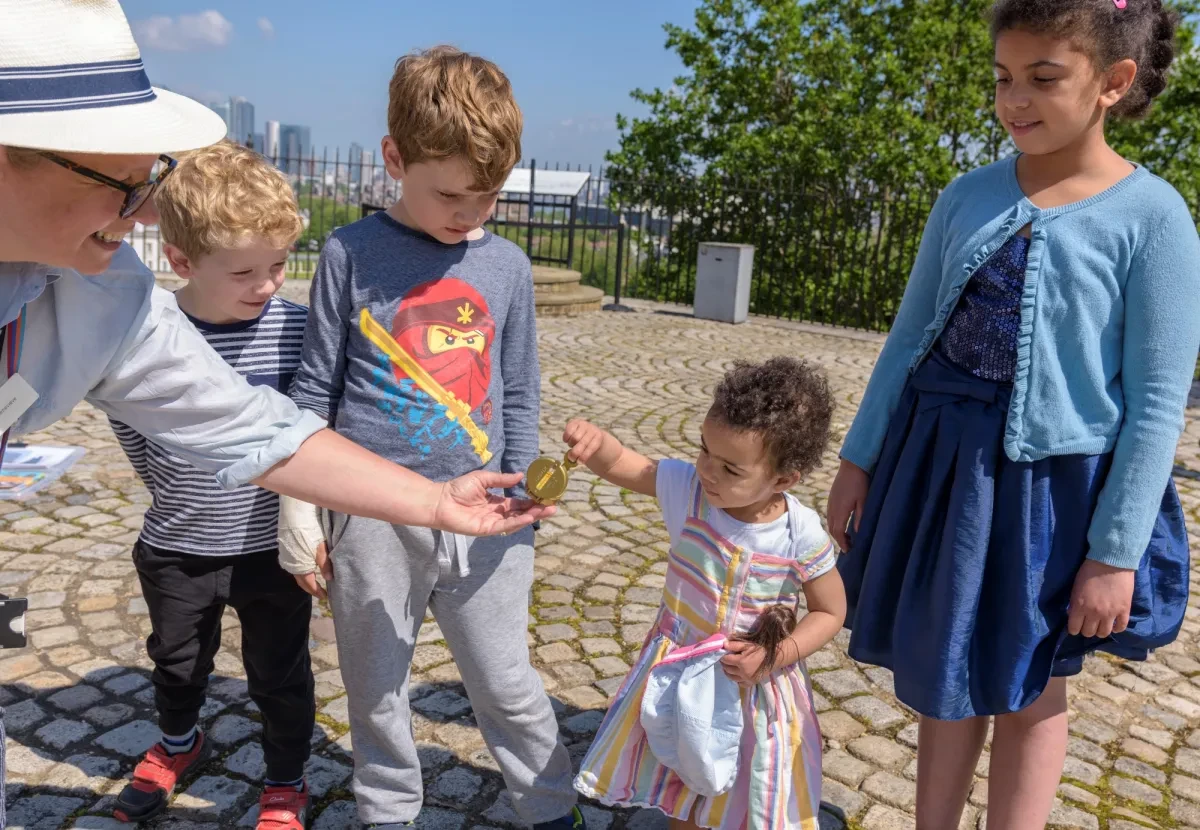 A young girl delicately holds a compass held by a staff member at Royal Observatory Greenwich