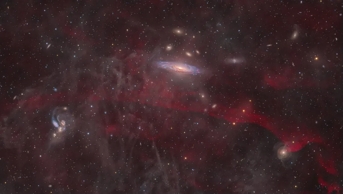 Swirling stars, nebulae and red emissions in a dark sky.