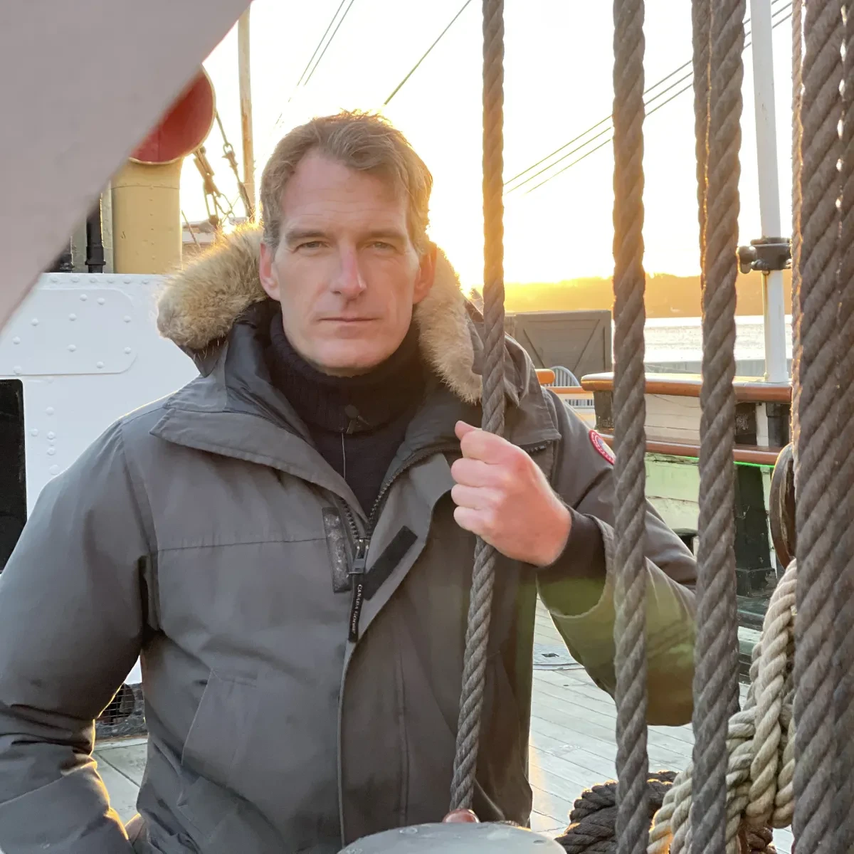 A portrait photograph of historian and presenter Dan Snow. He is on the deck of a ship, holding a rope and staring seriously into the camera