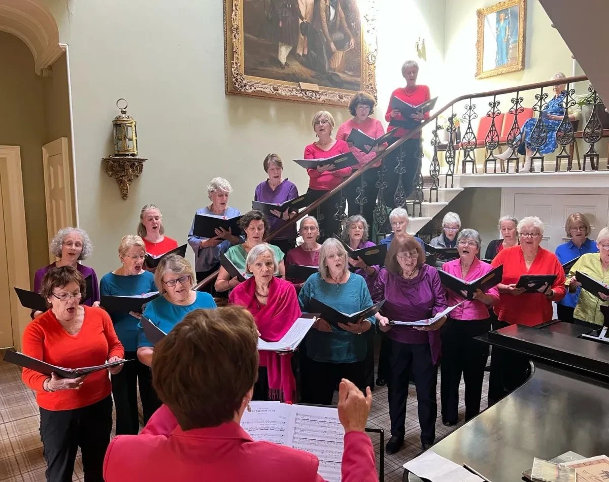 Photo of choir with lots of people standing on the steps of a regal building and singing