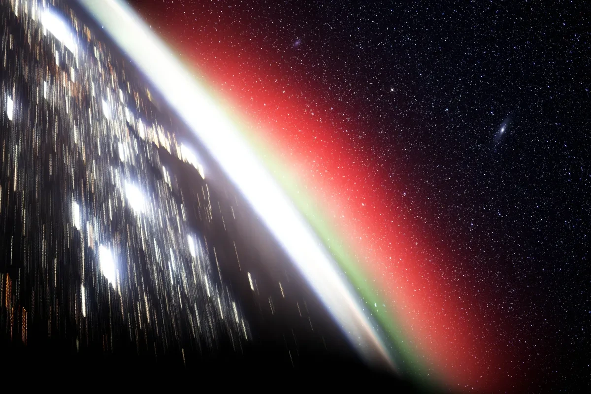 Photo taken from International Space Station looking at the Earth with silver lights on it, with green and pink aurorae on the horizon and lots of stars in space