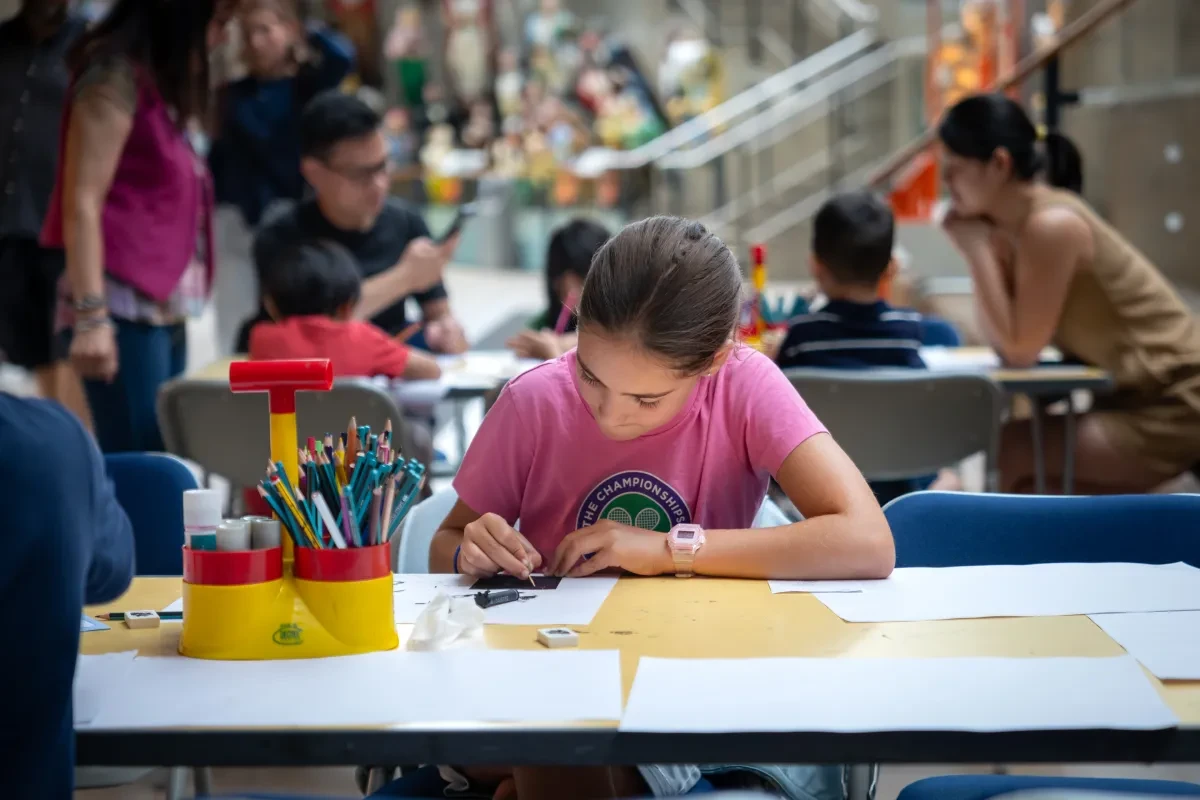 A child colours in at a table underneath the hull of Cutty Sark