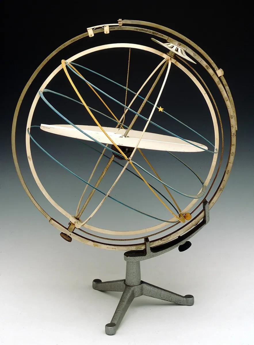 Armillary sphere. The primary sphere consists of six metal rings. Between the primary sphere and the meridian ring, there is a movable metal semicircle fixed to the poles. A small yellow wooden square acts as a sliding indicator. Attached to the meridian ring, there is a graduated altitude quadrant with a yellow altitude quadrant with a yellow star as a sliding indicator. The sphere with its meridian ring is sustained by a metal arm attached to the pillar of a metal tripod stand. 