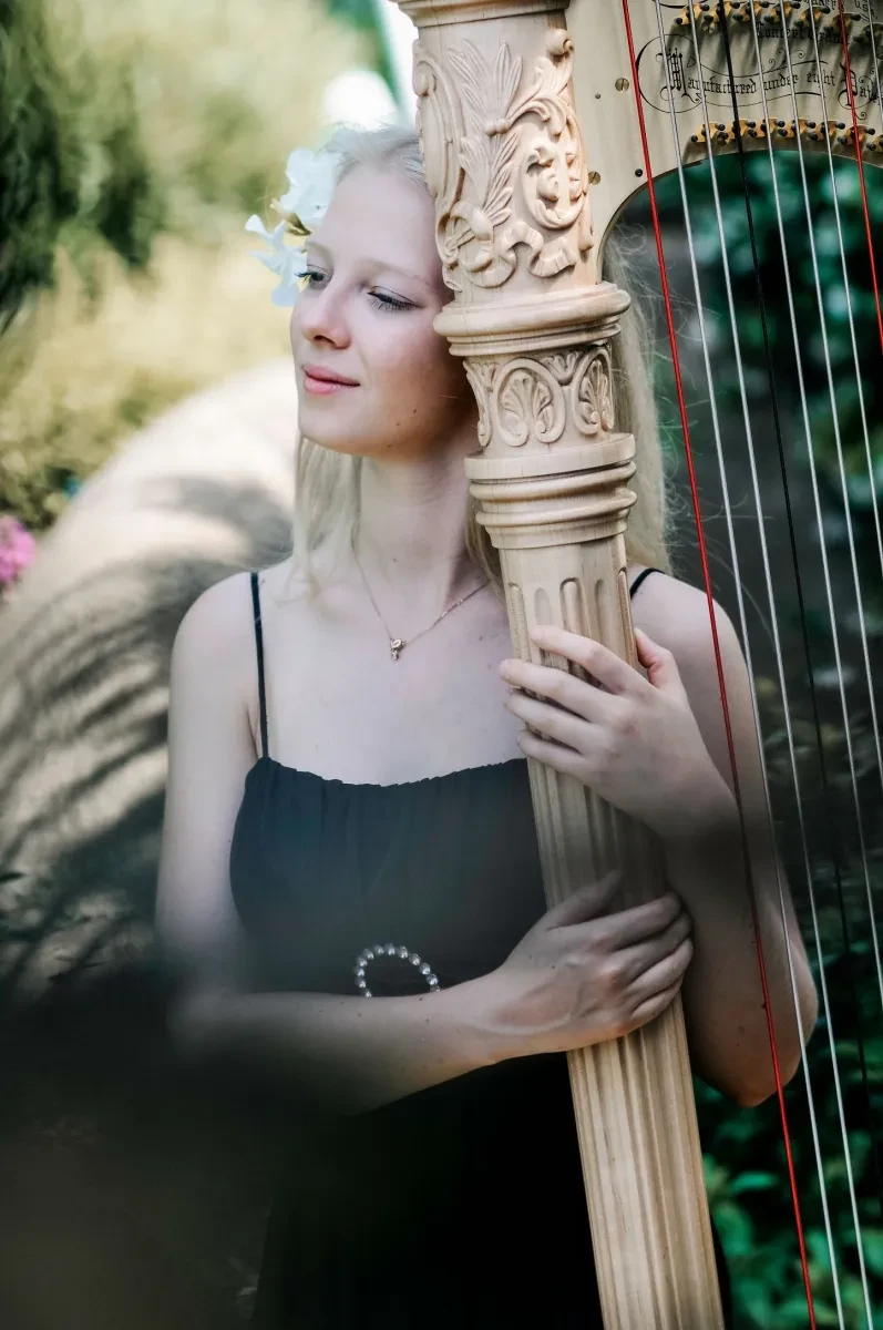 A woman wearing a black vest top rests her head on a golden harp