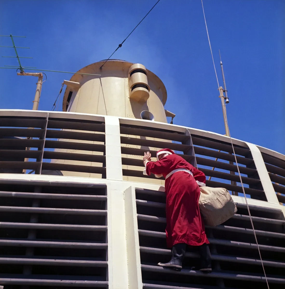 A crew member dressed as ’Father Christmas’ comes down the grille in front of the forward funnel on Christmas Day. 