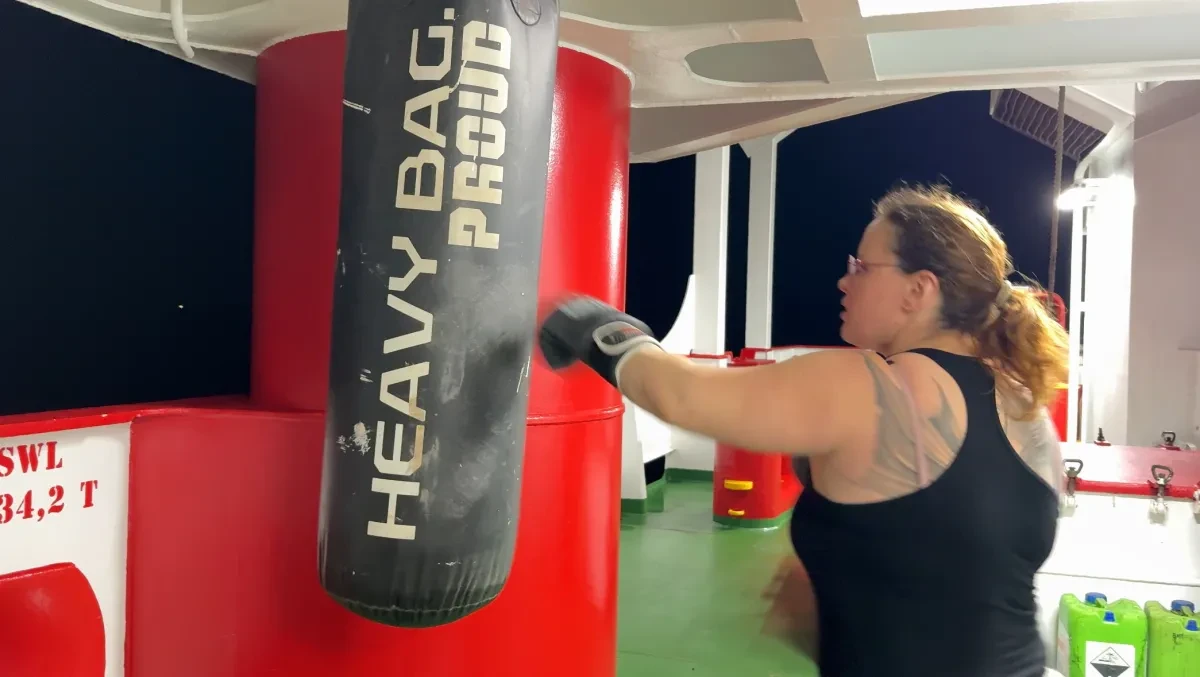 A woman wearing boxing gloves exercises with a punching bag on board a container ship