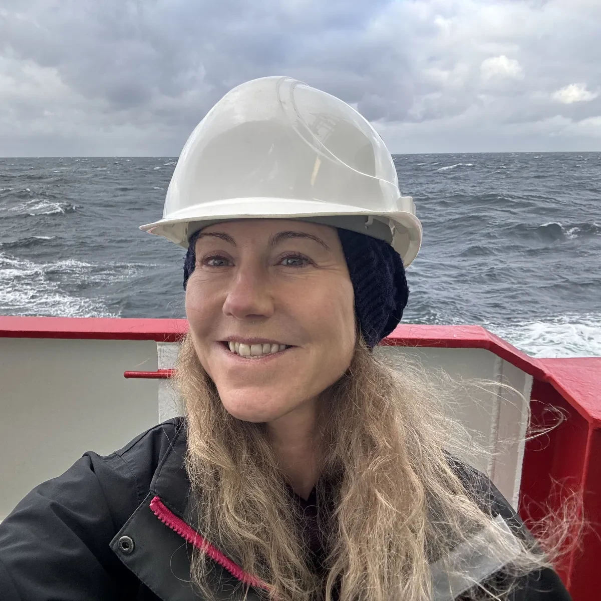 Researcher and artist Zoe Childerley takes a selfie on board a cargo ship. She is wearing a white hard hat and smiling