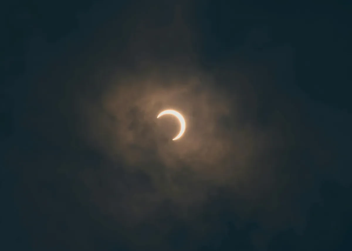A partial solar eclipse visible through a hazy sky, with the sun appearing as a bright crescent