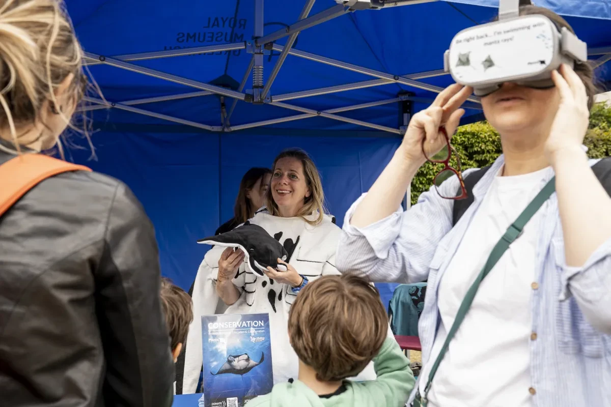 People gathered round a science stall about manta rays. A person in the foreground is looking through a VR headset