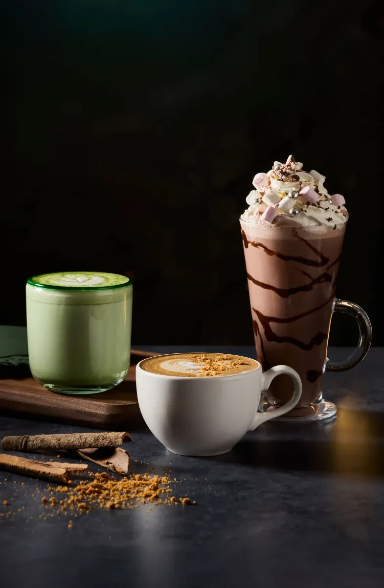 A light green matcha latte, a short coffee cup and a tall hot chocolate with white whipped cream on top.