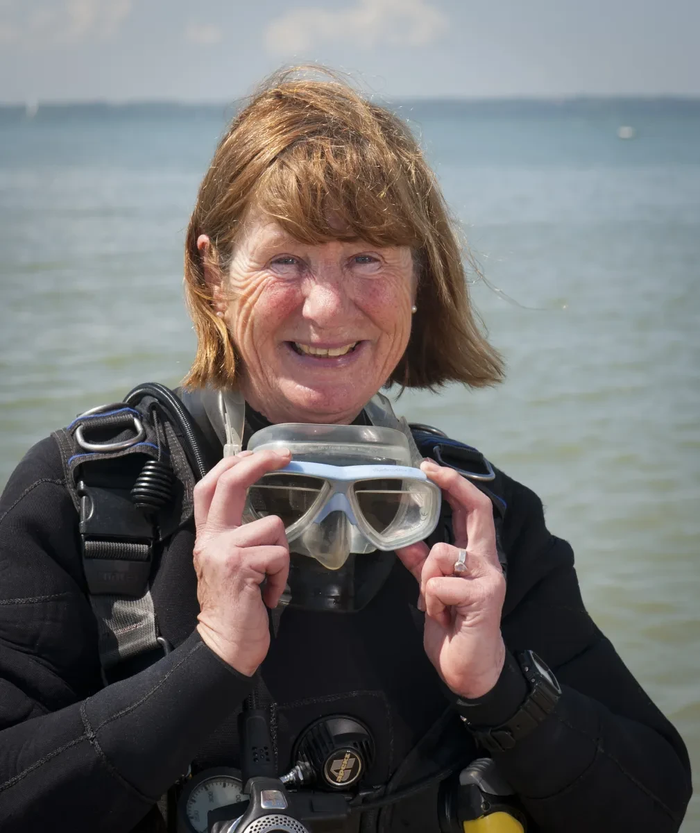 Headshot of maritime archaeologist Jane Maddocks wearing a dive suit and standing on a beach