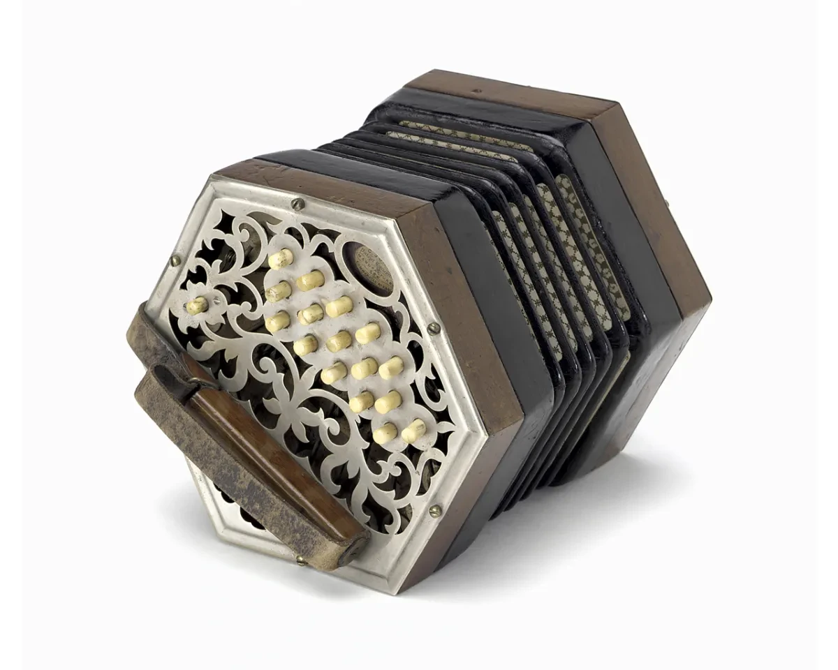 A hexagonal concertina with white buttons, a brown strap, a brown wooden case and a decorative metal inlay facing forwards