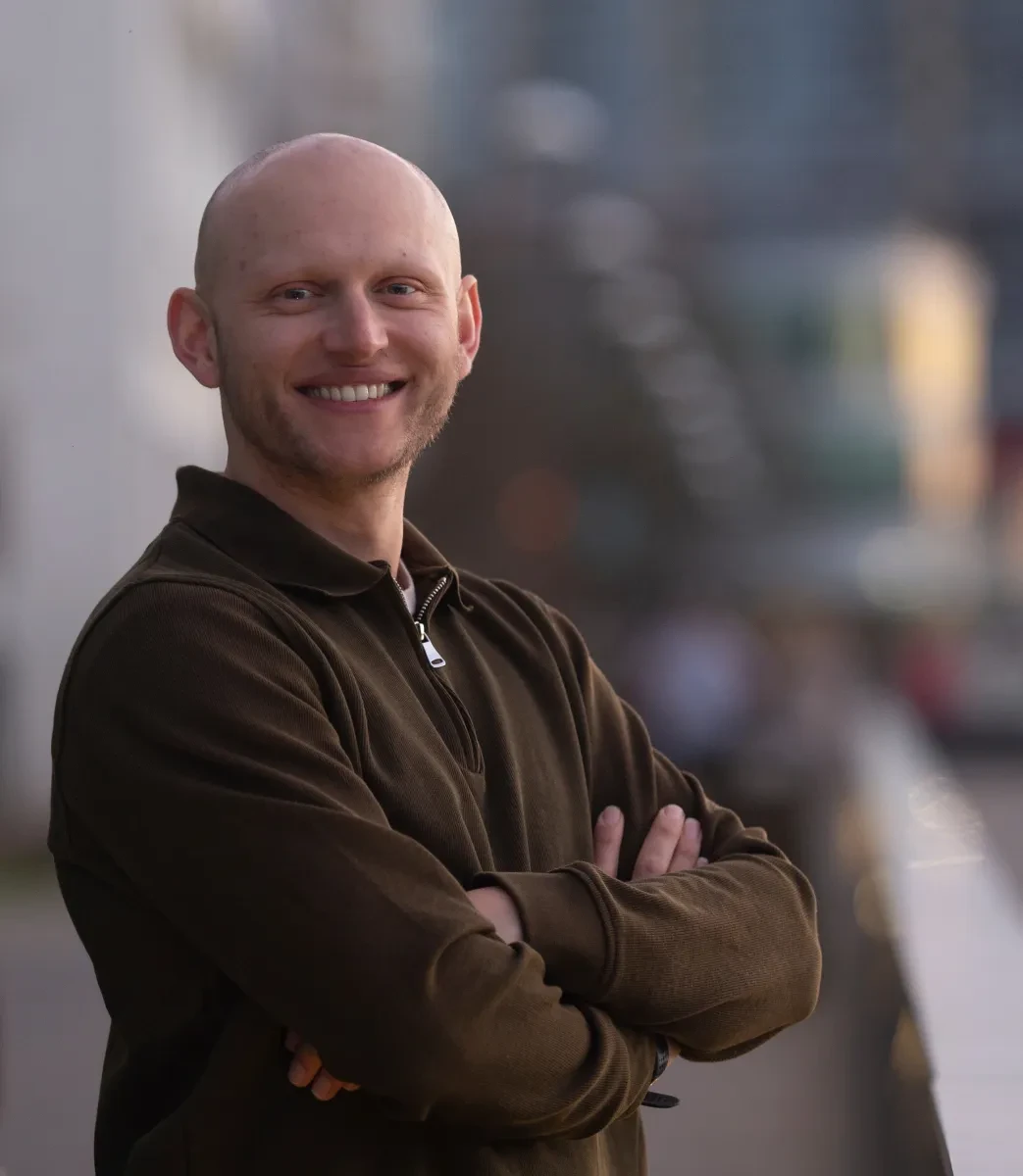 Photo of Gideon Bendavid-Walker with arms crossed smiling at the camera