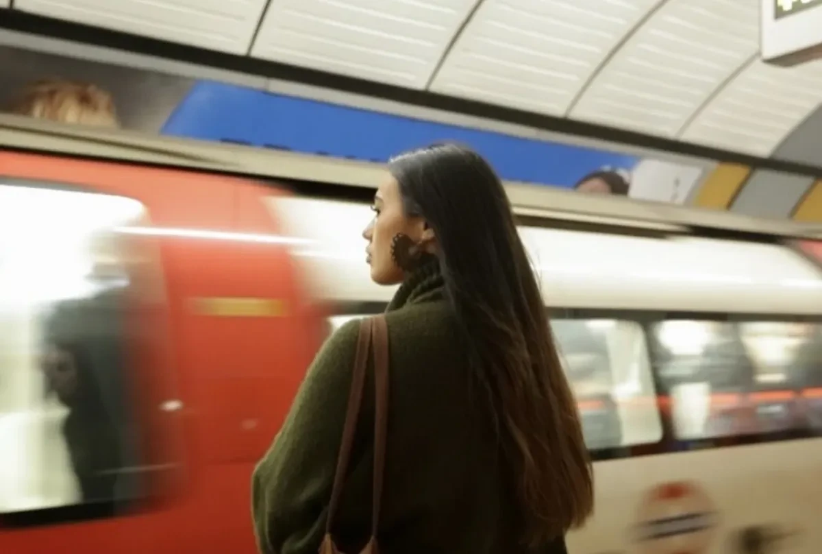 A woman with long black hair wearing large earrings, stands waiting for a Tube train on the London Underground