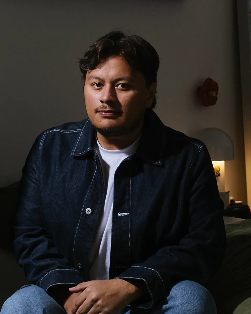A young man in a white shirt and a blue jacket looks thoughtfully out of his portrait photograph.