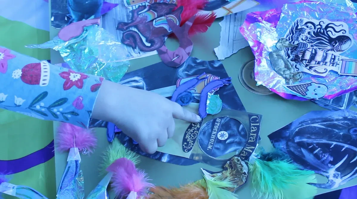 Photo of a child's hand pointing at some collaged materials