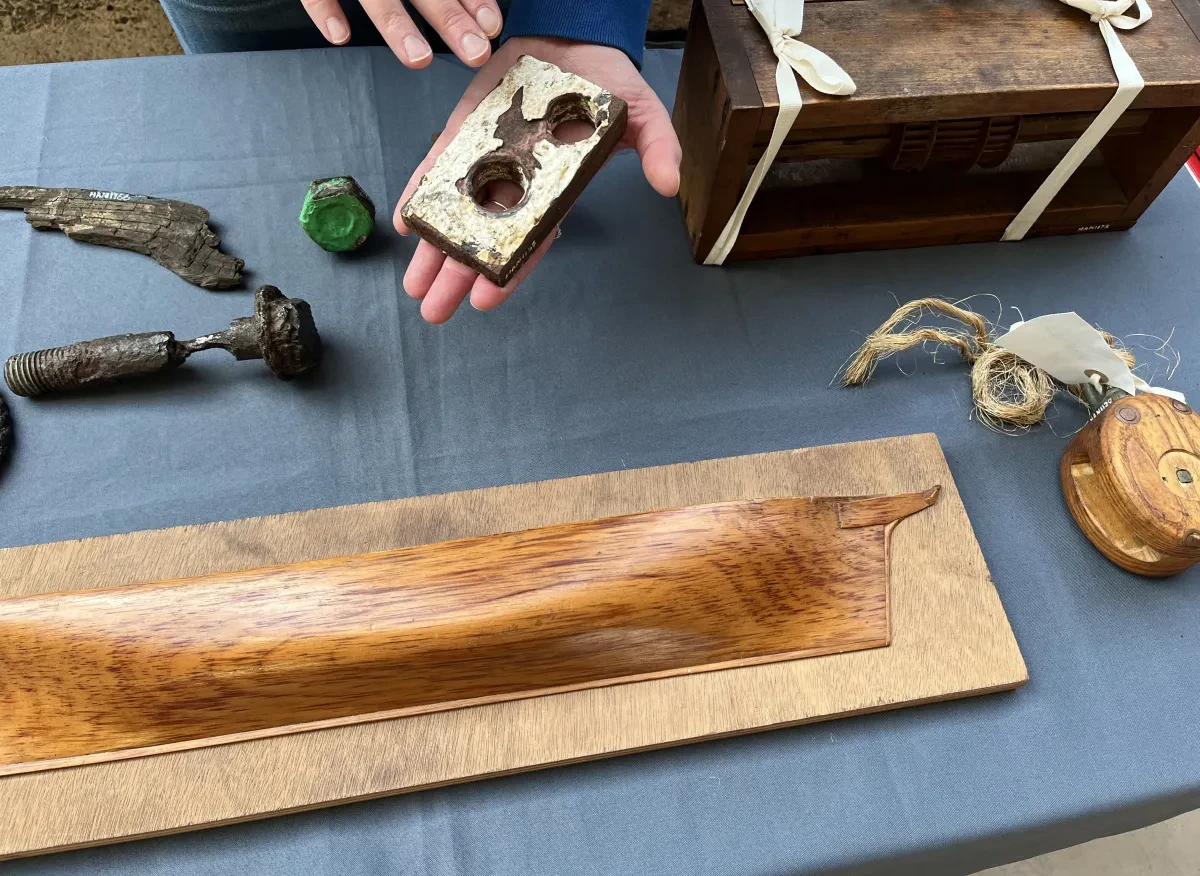 Photo of assorted objects including wooden hull model piece and a ship block