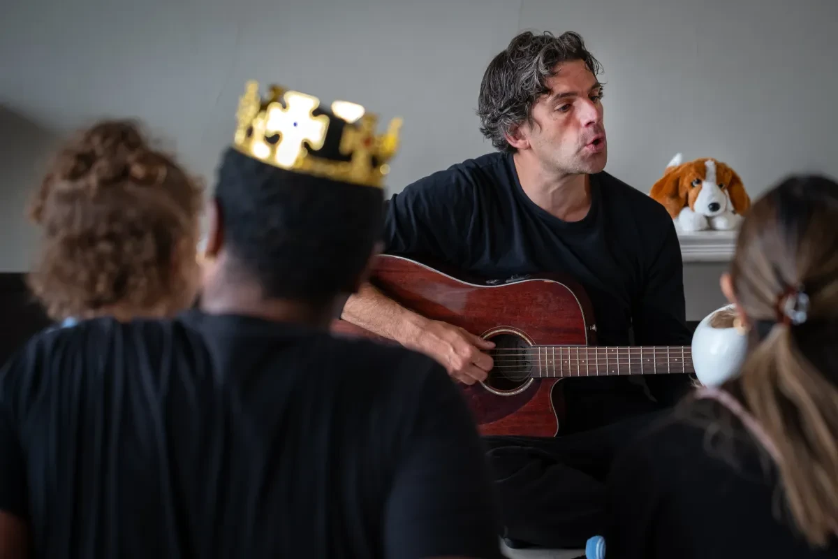 A man plays guitar in the Queen's House surrounded by children in fancy dress