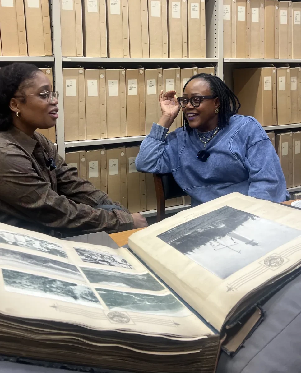 Sharon Walters and Nydia A. Swaby sit in front of a large manuscript in a room filled with archival boxes