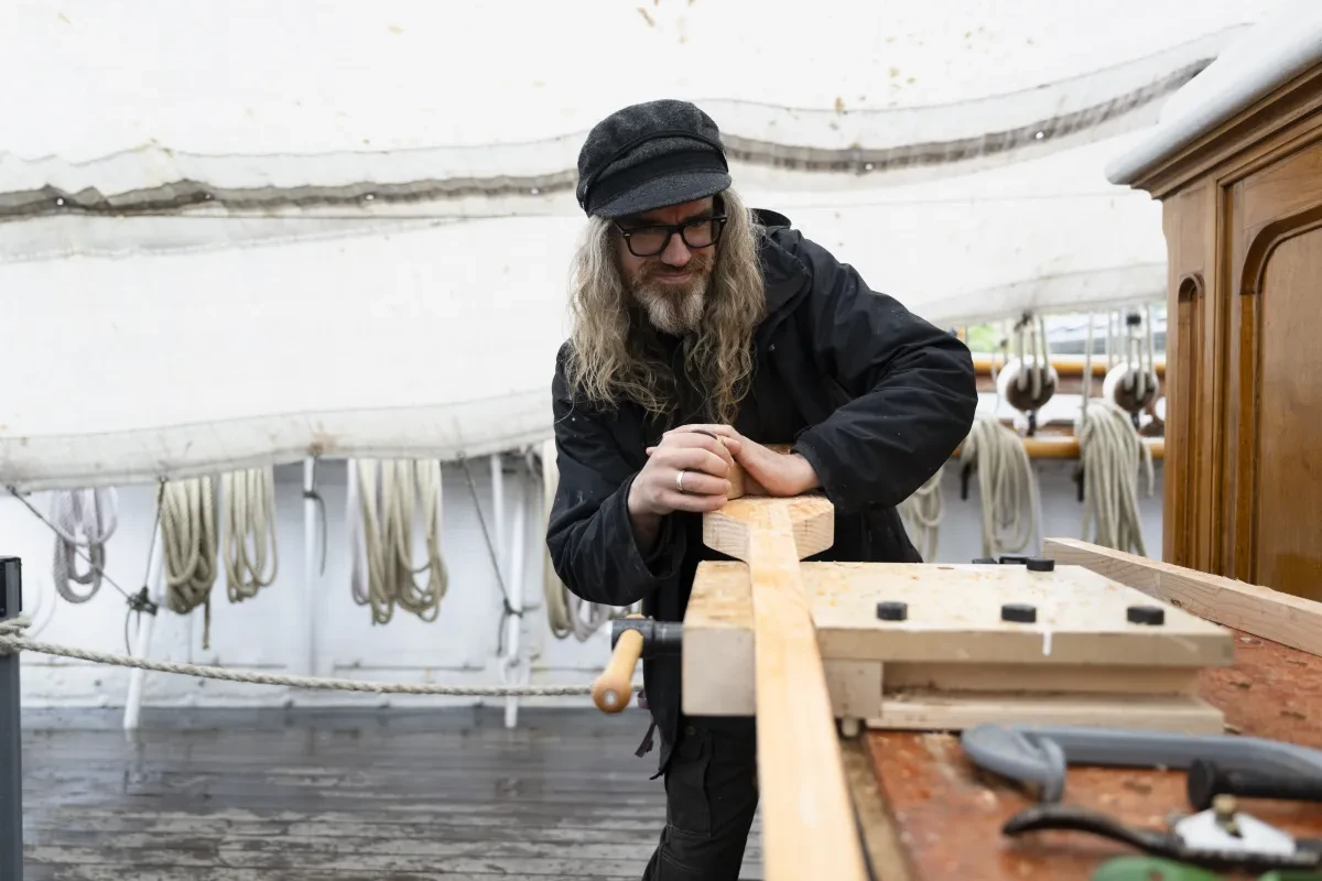 A man sanding a wooden oar which is lying flat on a table