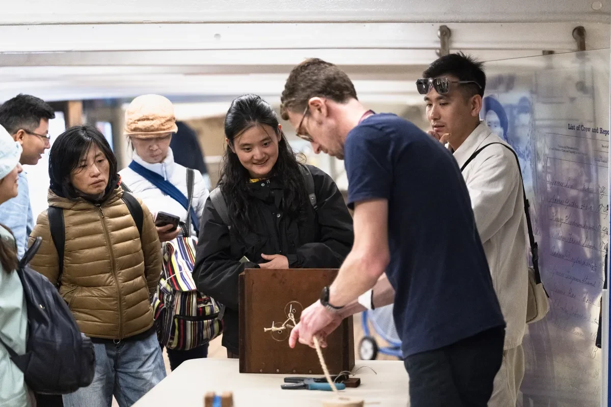 A Cutty Sark visitor assistant demonstrating a small, simple rope making machine to some visitors
