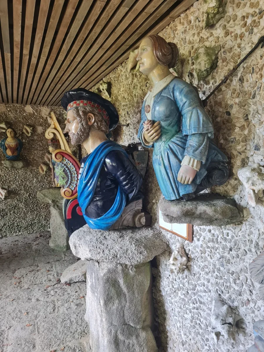 Two figureheads on display in a stone shed; one is a bearded man with blue painted clothing; the other is a woman in a light blue dress