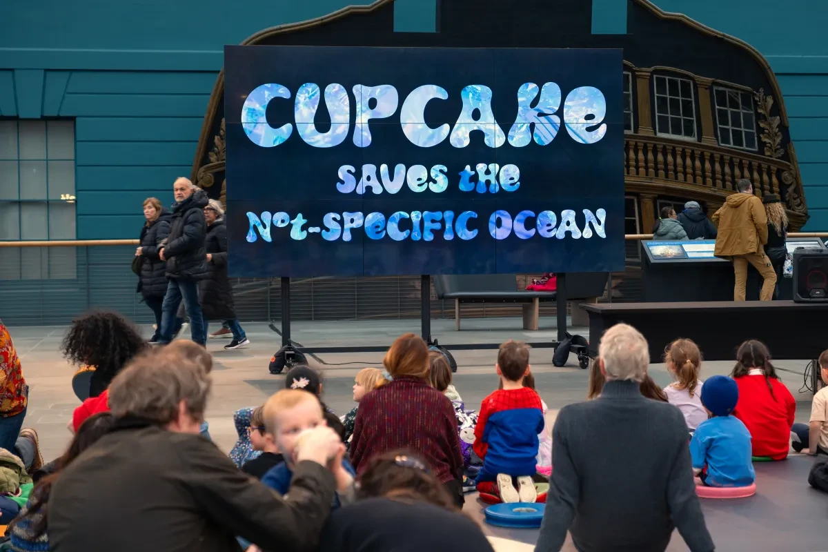 Photo of a large tv screen on the Ocean Map with Cupcake saves the none specific ocean written on it and a crowd of families watching in front