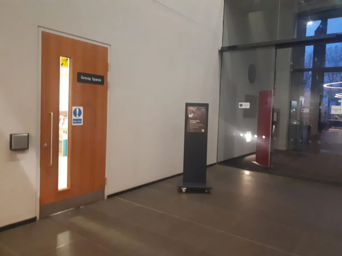 Photo of the door into the Group Space with a metal power assisted button, directly to the left of the door. A sign on the door say Group Space