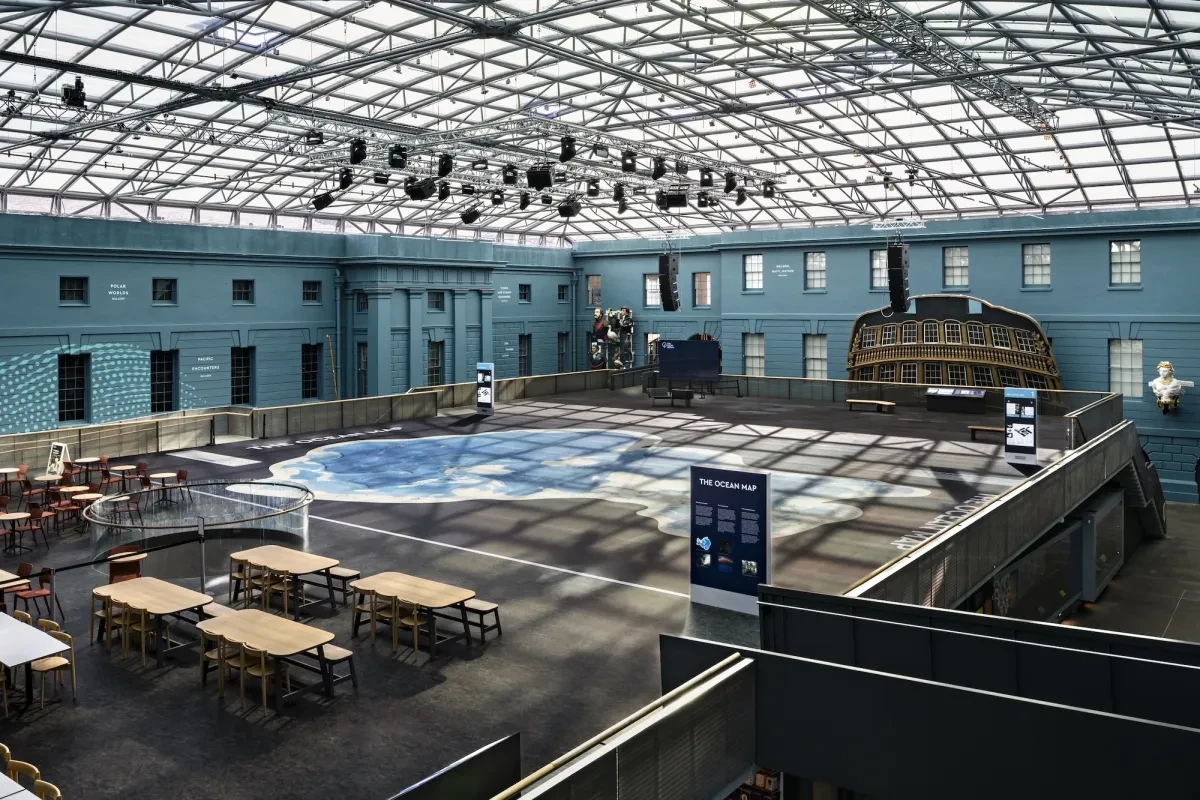 A scene showing the main 'Ocean Court' area of the National Maritime Museum outside of visitor hours. The space is large, with a domed glass ceiling and blue-painted walls